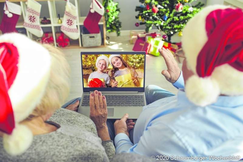 Staying at home during quarantine, Christmas in self-isolation, virtual family meeting. Happy grandparents in Santa hats sitting on sofa together video calling grandchildren. Back view over shoulder