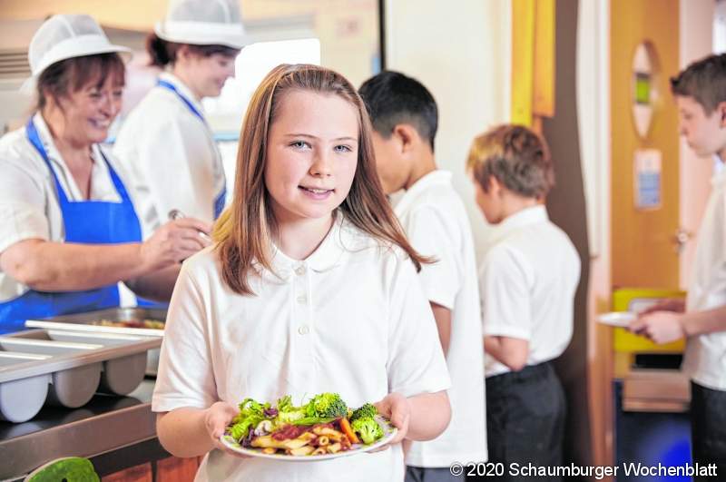 Girl holds a plate of food in school cafeteria, head turned