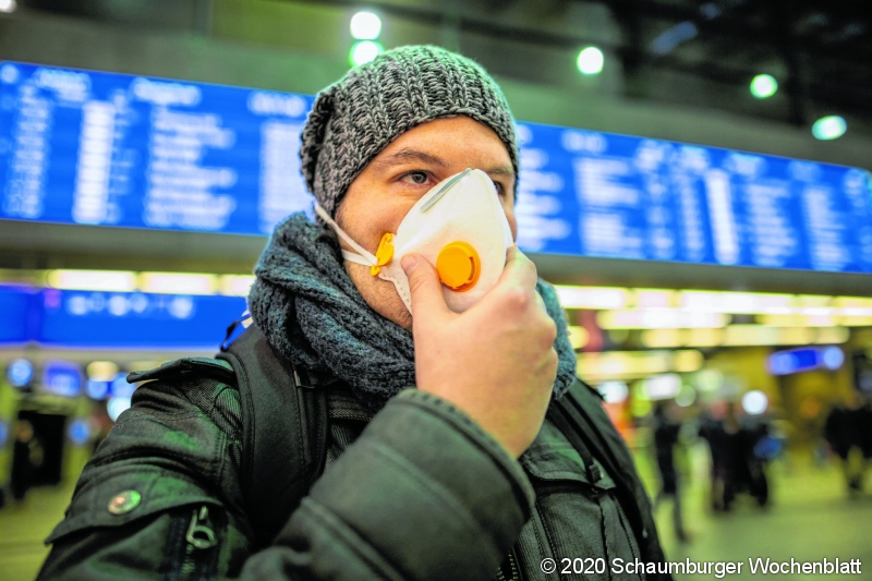 Man wearing a respirator mask device for health protection at an airport or railway train station in a crowd of people while travelling. Epidemic corona virus infection, flu sickness and travel illness concept.