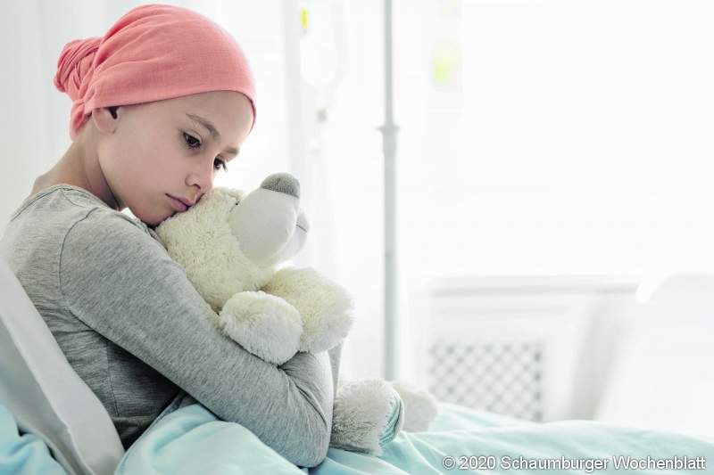 Weak girl with cancer wearing pink headscarf and hugging teddy bear